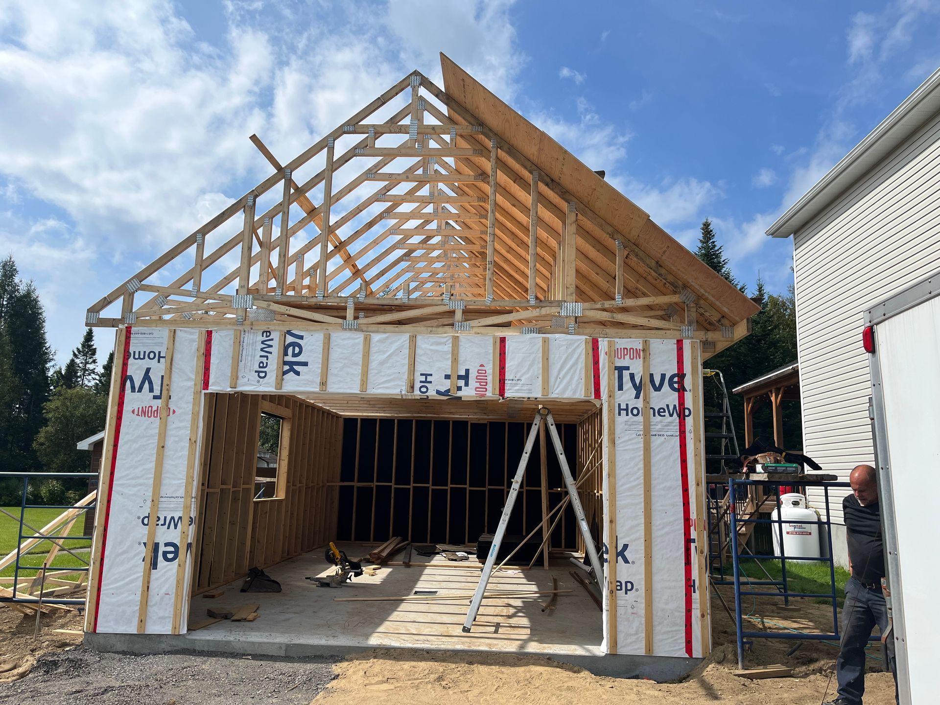 Garage en construction, à ossature bois, recouvert d'une bâche Tyvek blanche, sous un ciel bleu.