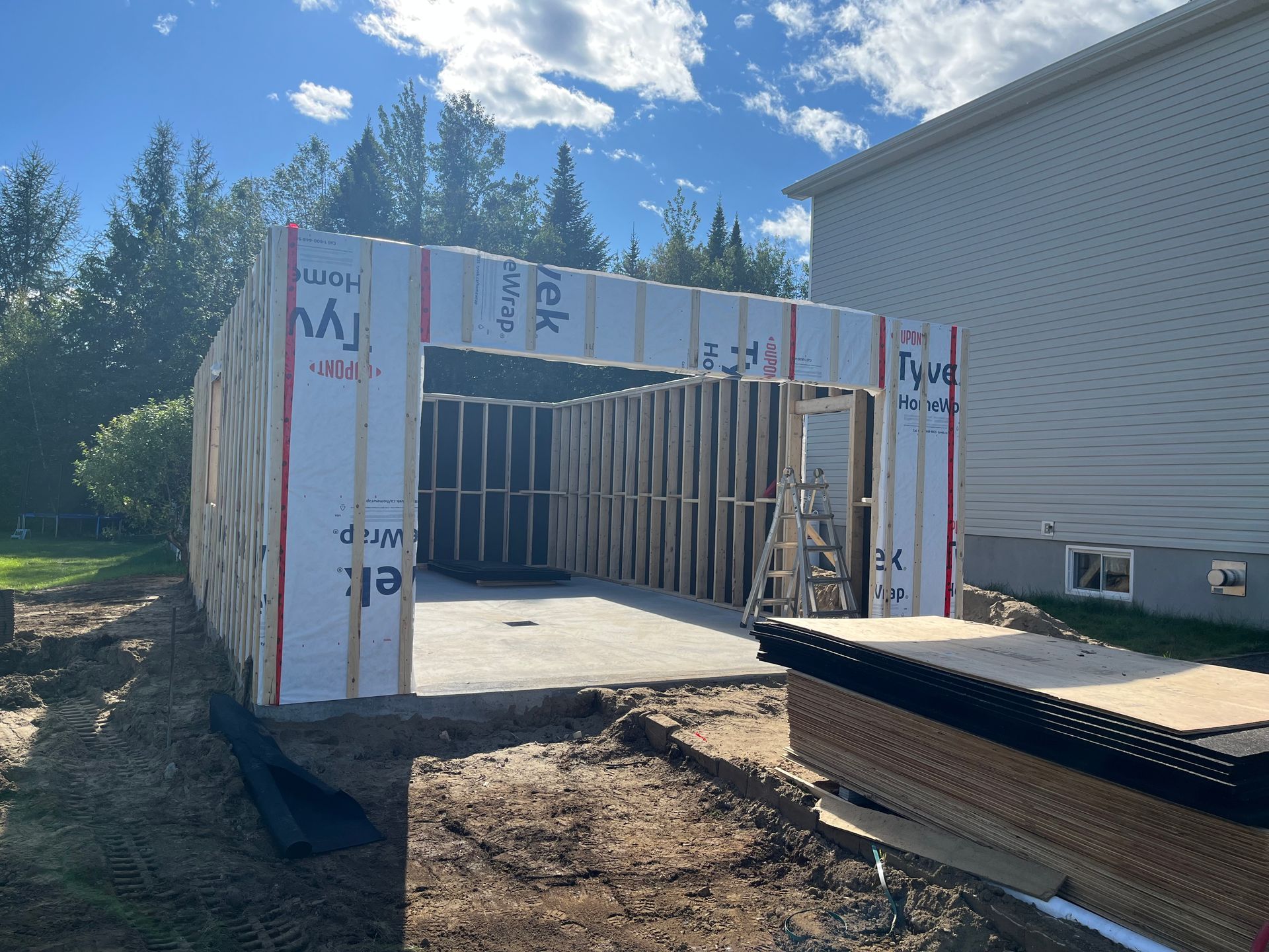 Structure à ossature bois en construction, entourée de pelouse et d'une maison.