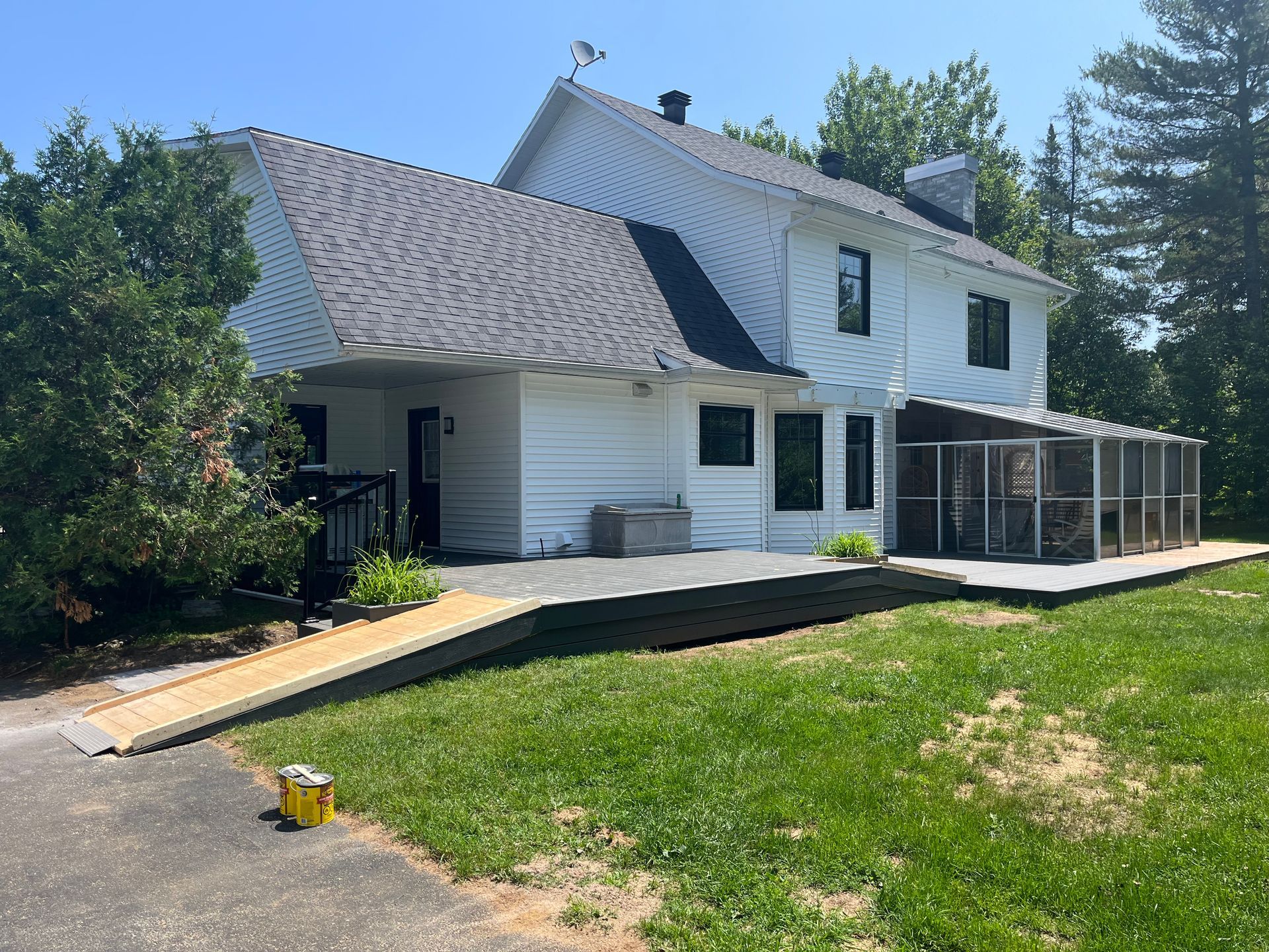 Maison blanche au toit foncé et rampe d'accès. Enclos pour chats à droite. Pelouse verte.
