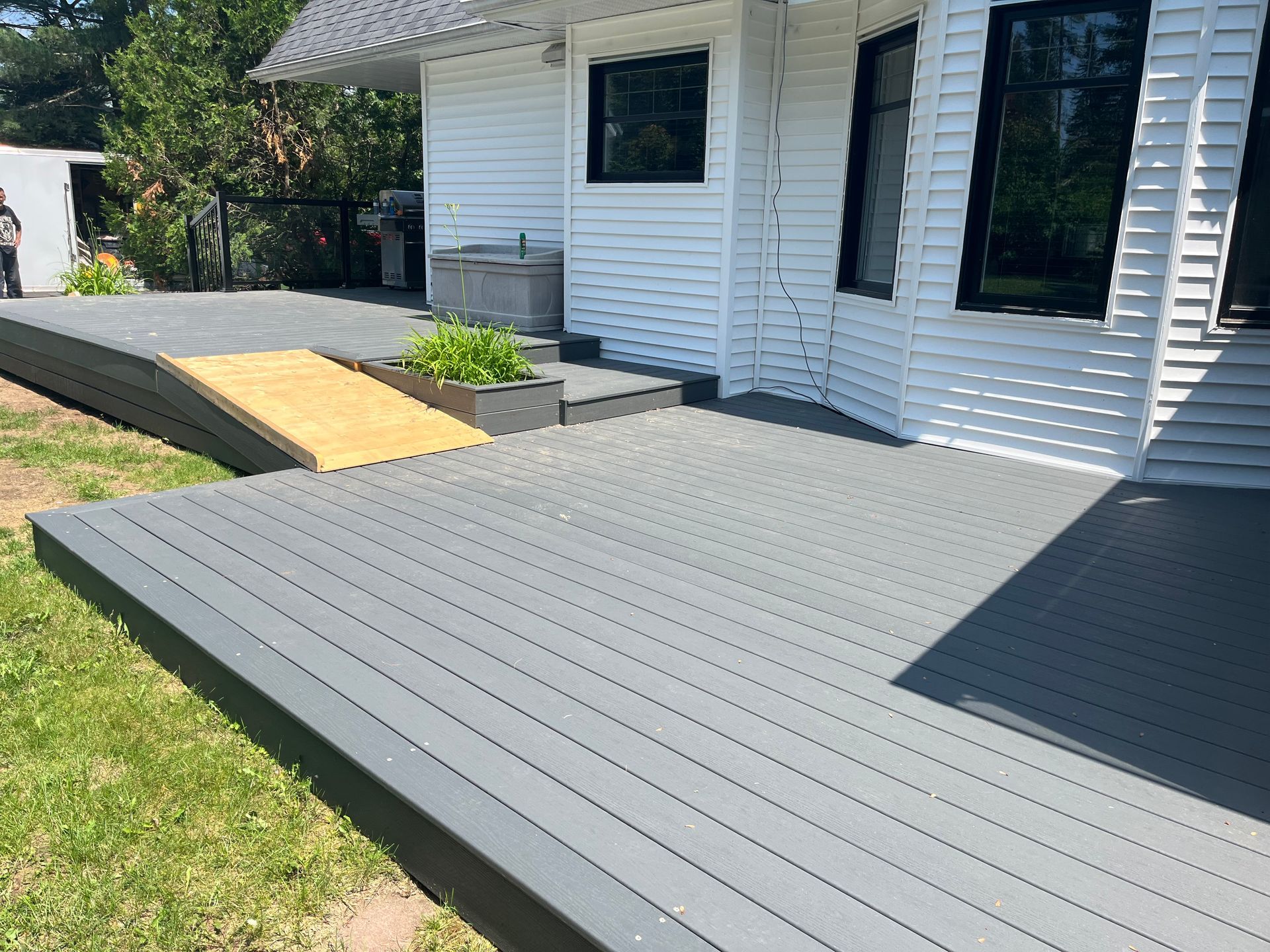 Une terrasse en composite gris avec une rampe jaune, menant à une maison blanche aux encadrements de fenêtres noirs.