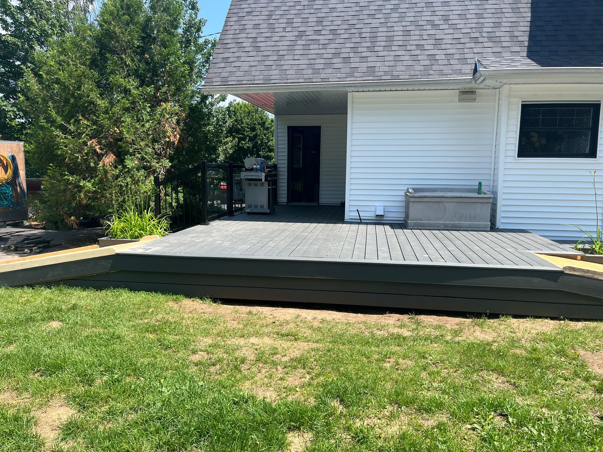 Terrasse arrière peinte en gris foncé, attenante à une maison blanche au toit anthracite.
