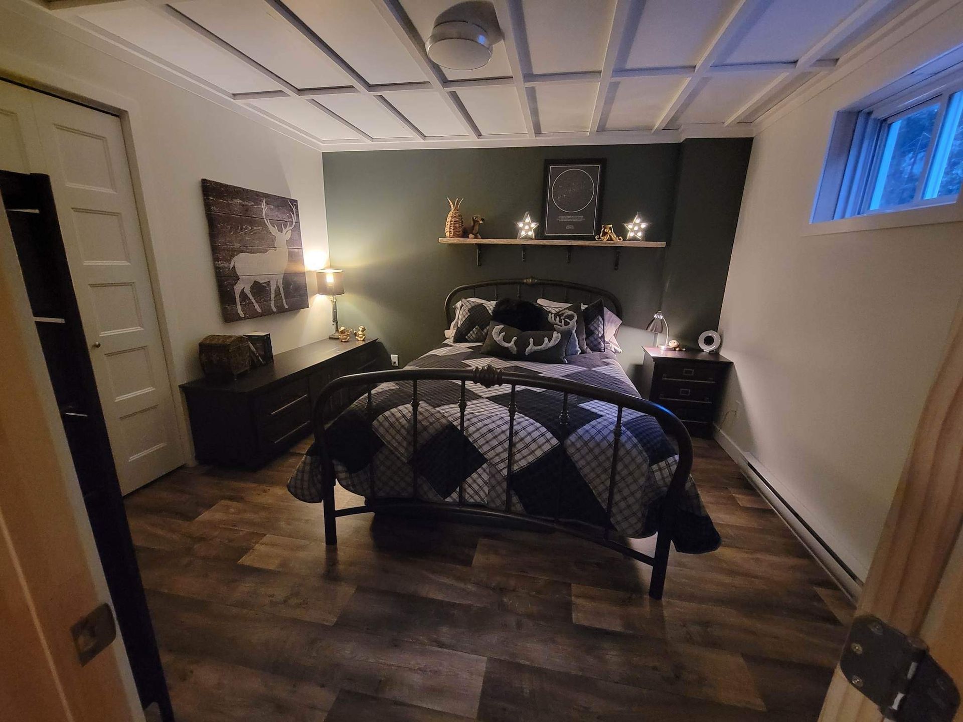 Chambre avec un mur d'accent vert foncé, un cadre de lit noir, un sol imitation bois et des objets décoratifs.