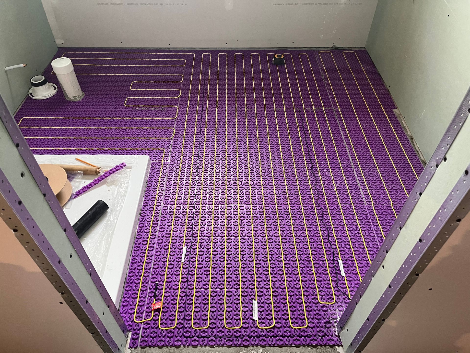 Des tubes de chauffage au sol violets sont installés dans une salle de bains en construction.