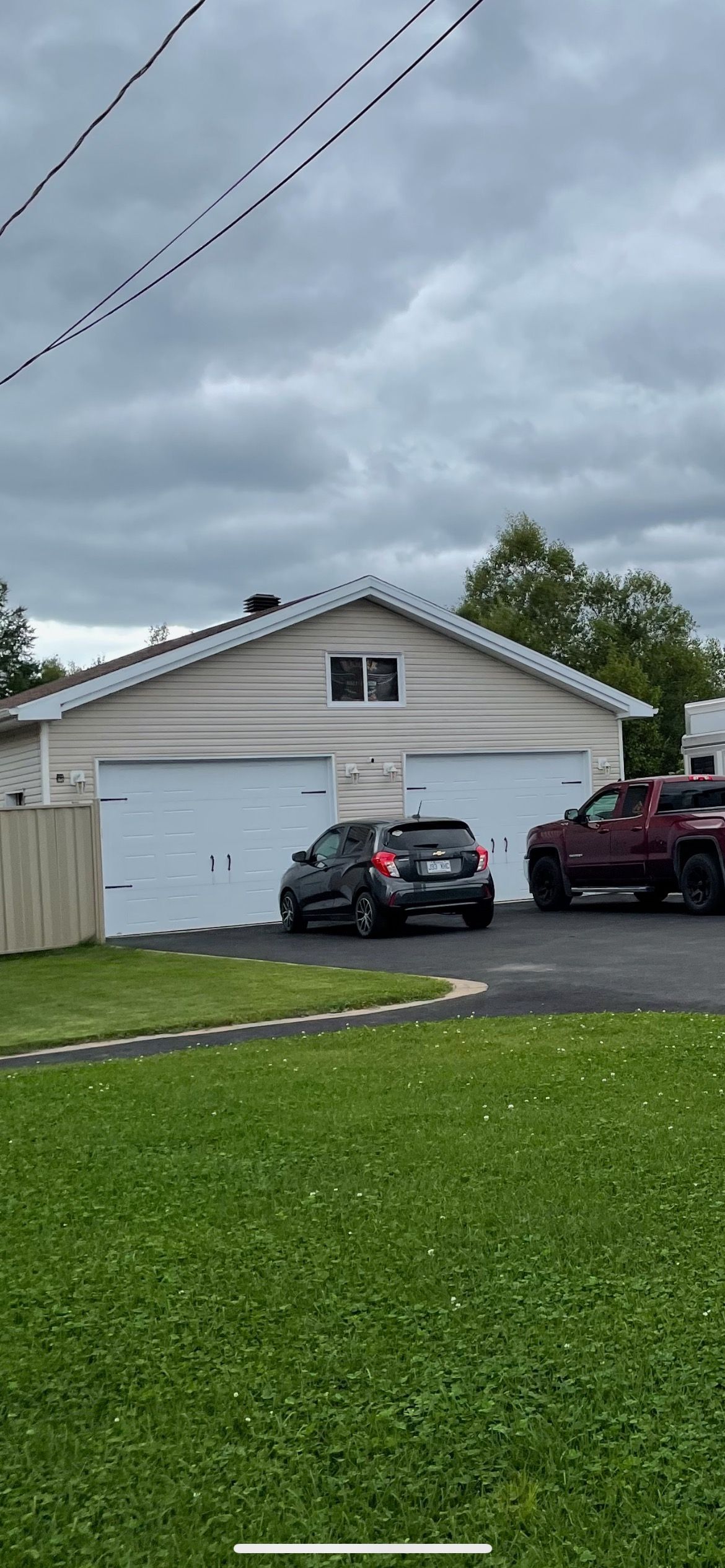Garage double avec portes blanches, voiture noire et camion rouge garés dans l'allée, ciel couvert.