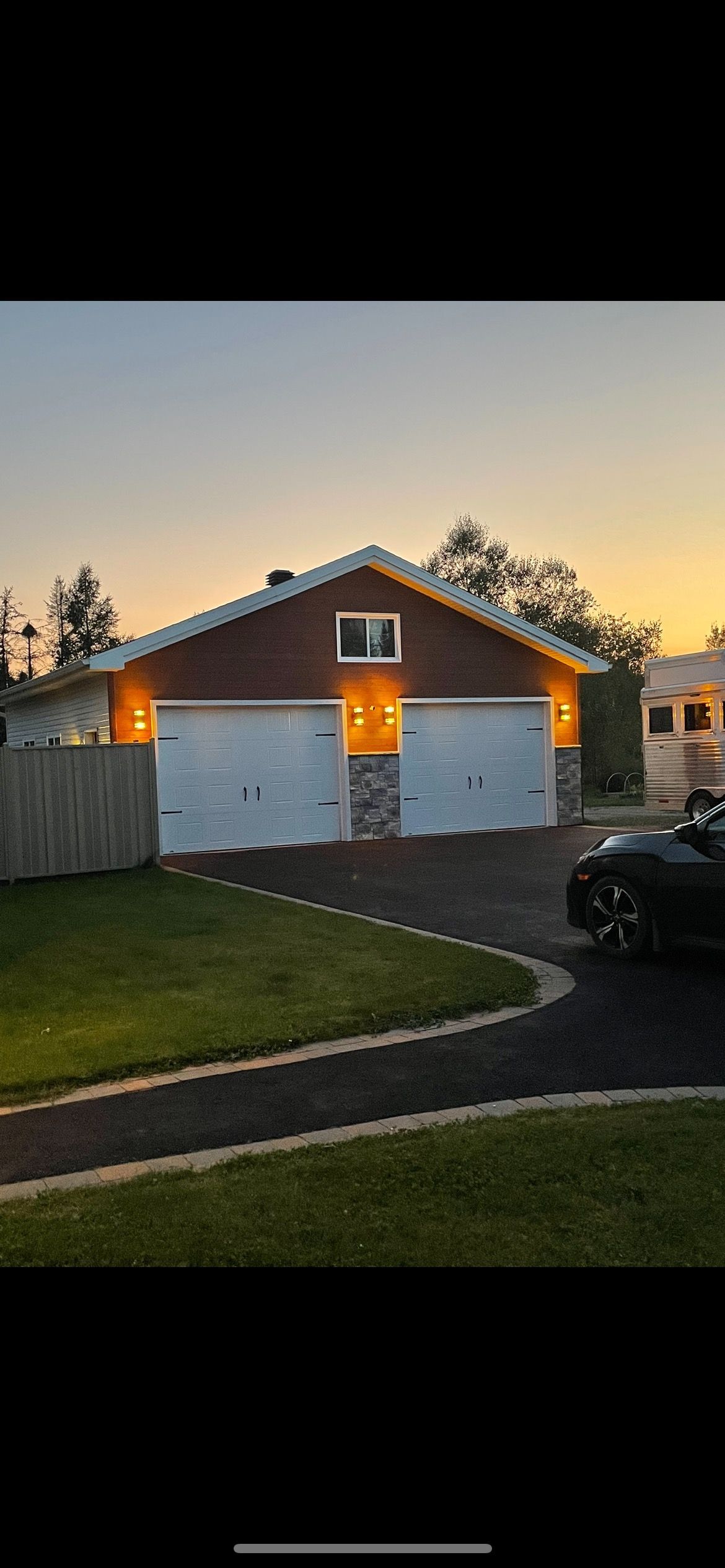 Garage avec deux portes blanches, façade en briques et éclairage. Allée et pelouse au premier plan.