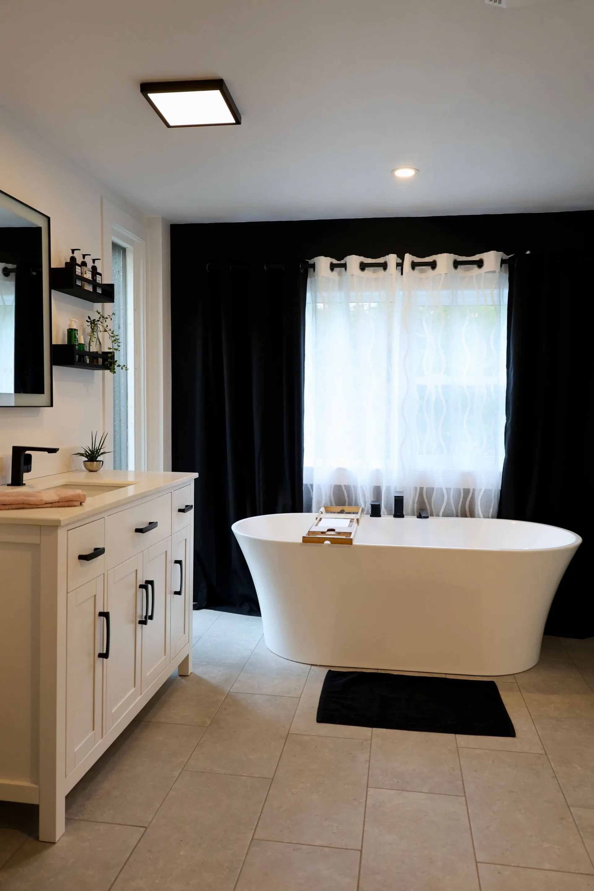 Salle de bains moderne blanche avec baignoire îlot, rideaux noirs et meuble-lavabo blanc.