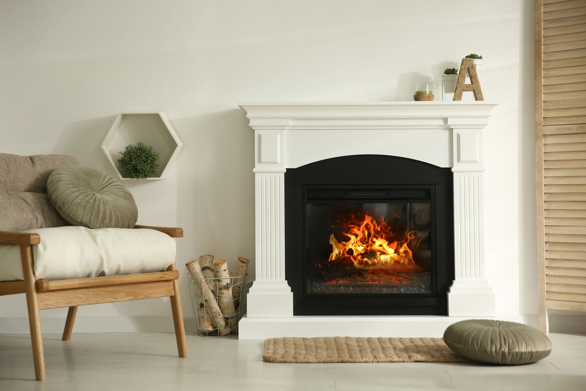 Fireplace in a white mantel with a burning fire, next to a chair and a wall shelf.