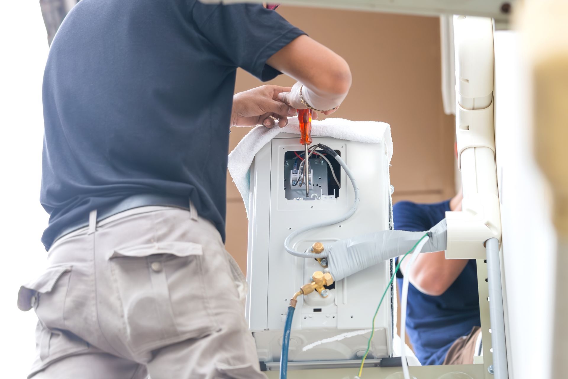 Technician installing an air conditioner unit with a screwdriver outdoors.
