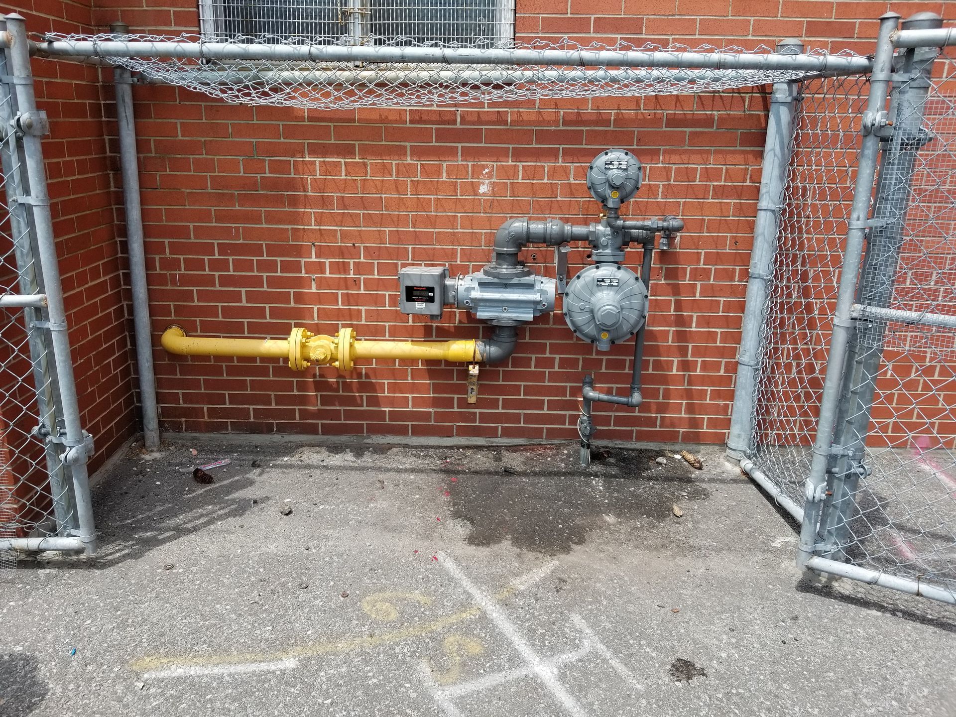 A brick wall with a fence and a gas meter on it