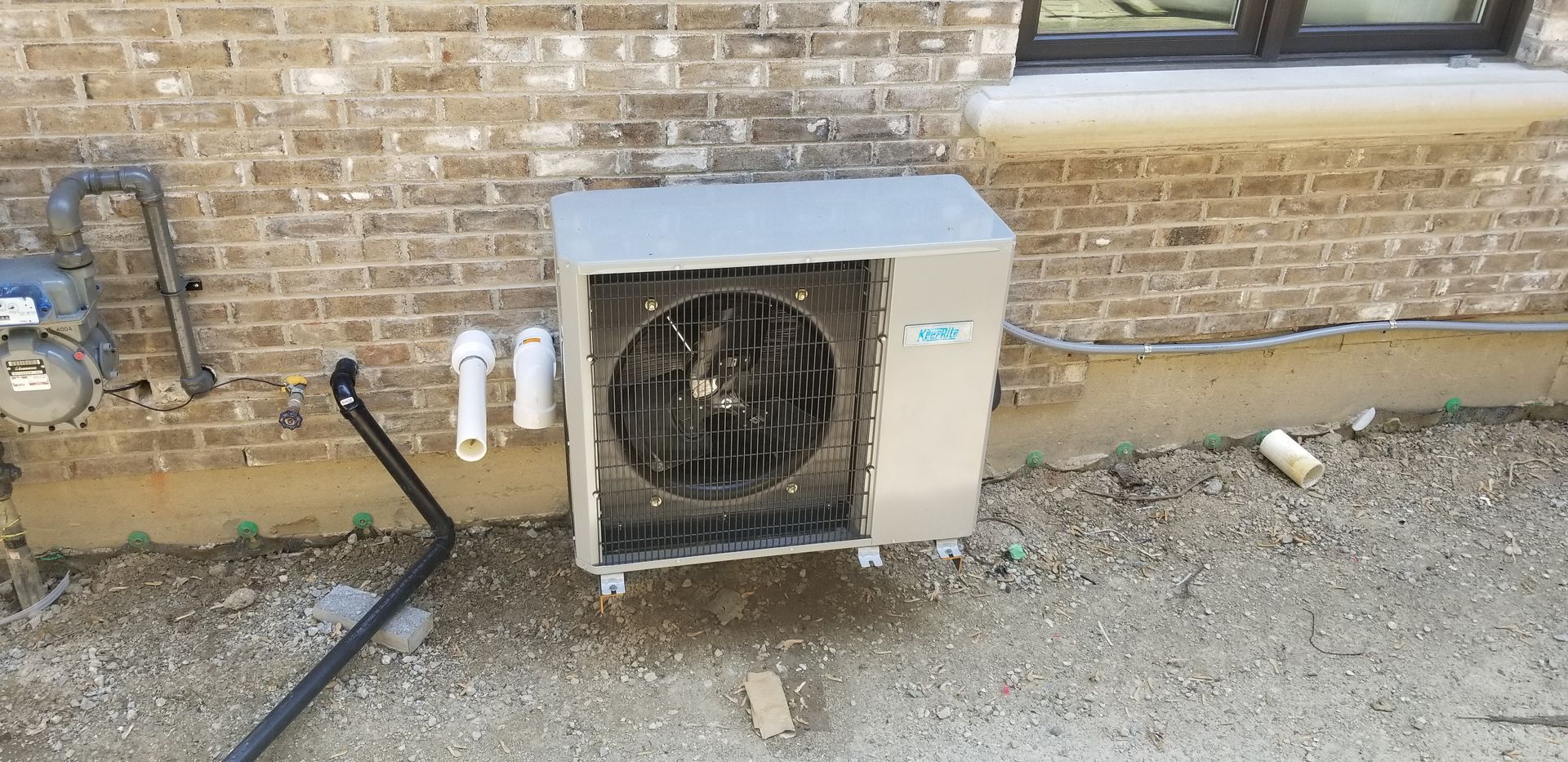 A broken air conditioner is sitting on the side of a brick building.