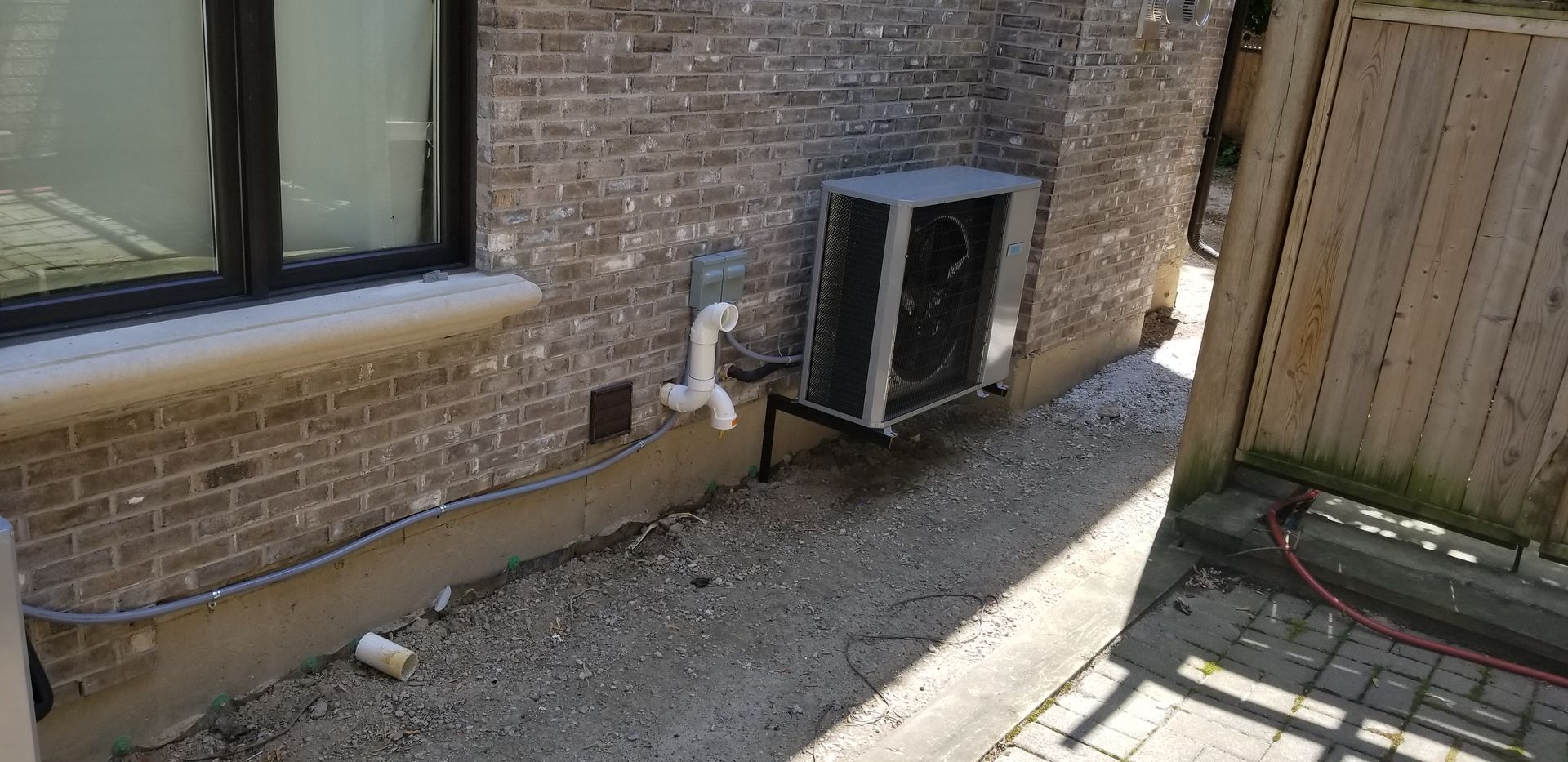 A large air conditioner is sitting on the side of a brick building next to a window.