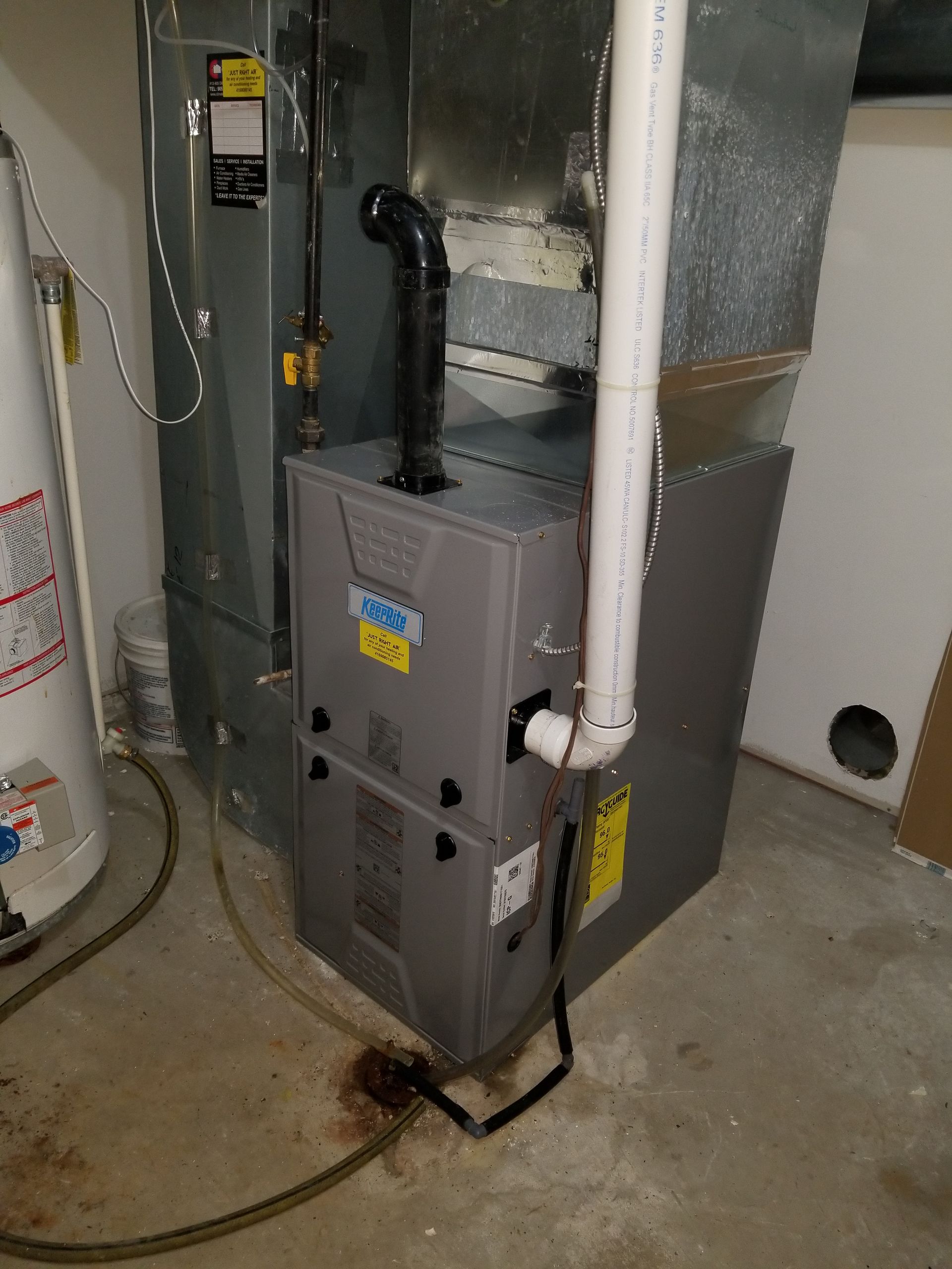 A furnace is sitting in a basement next to a water heater.