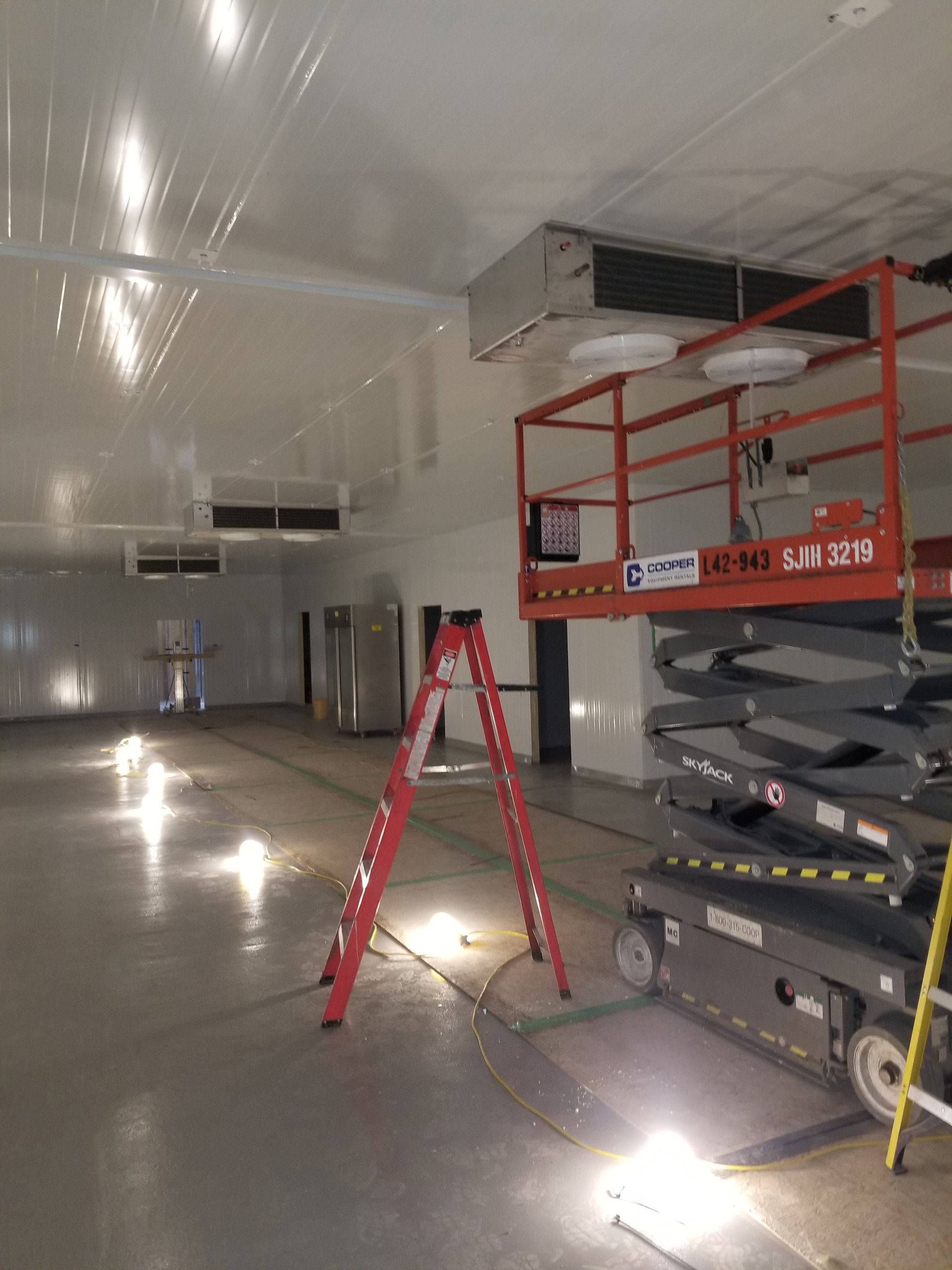 A large empty room with a ladder and a scissor lift.