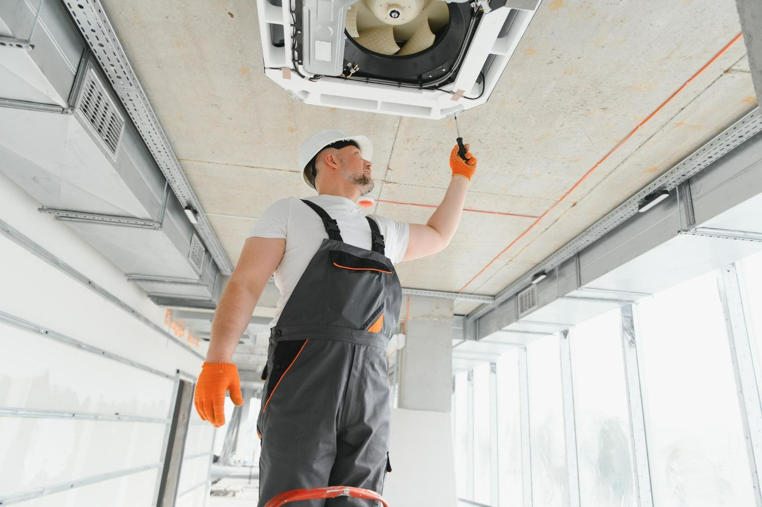 Worker on a ladder, installing HVAC unit on a construction site.