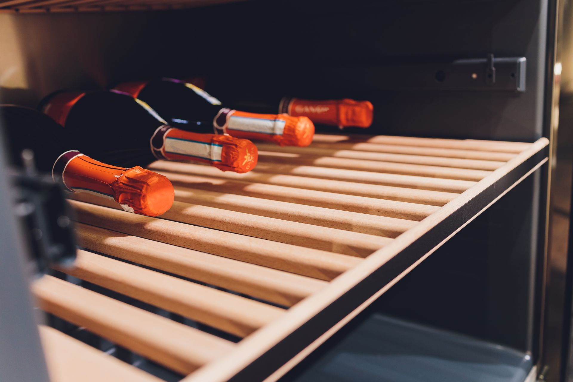 Wine bottles on a wooden shelf inside a wine refrigerator.