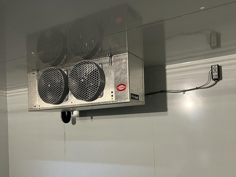 a refrigerator with two fans hanging from the ceiling in a room .