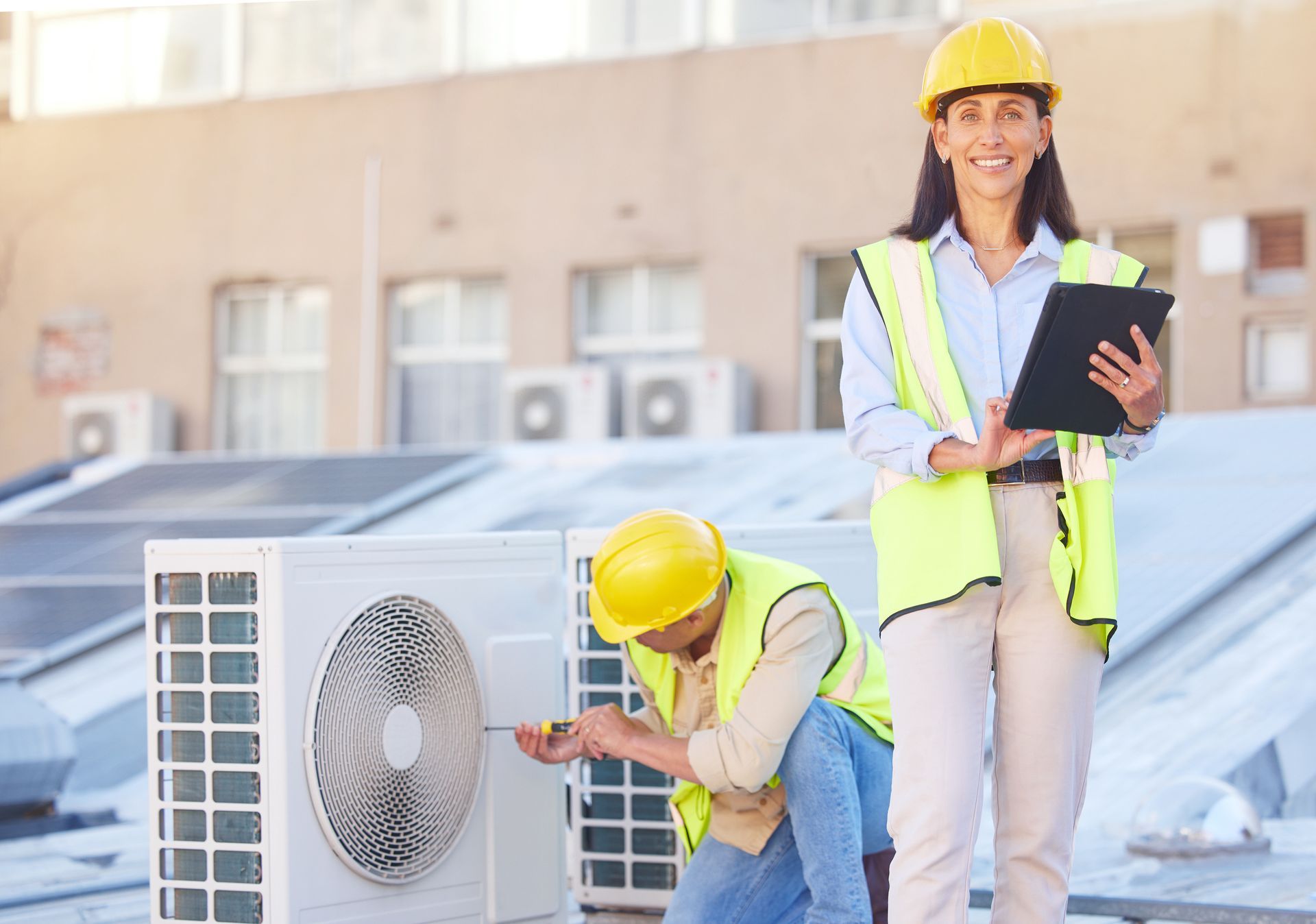 a man and a woman are working on an air conditioner on the roof of a building .