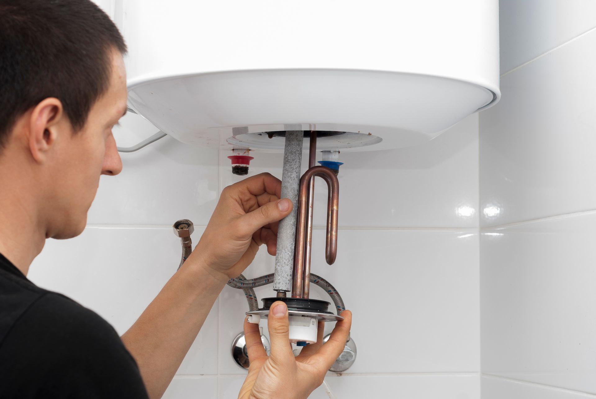 Man installing water heater component in a bathroom with white tiles.