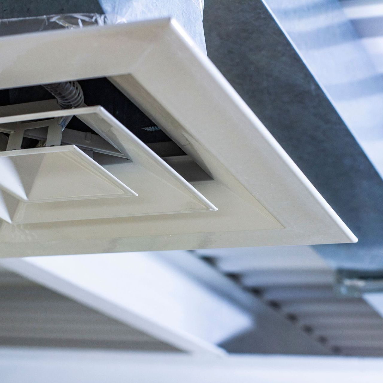 White ceiling air vent with angled vanes, installed in a duct.