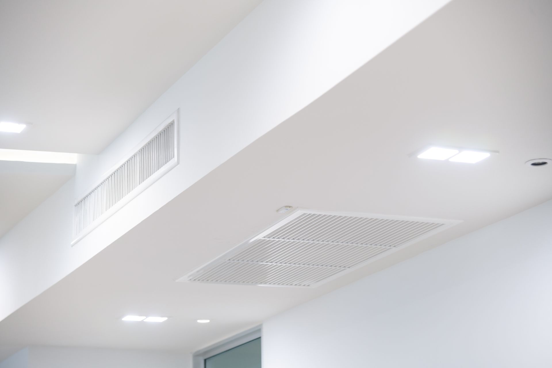 White ceiling with recessed lighting, ventilation vents, and a square air filter.
