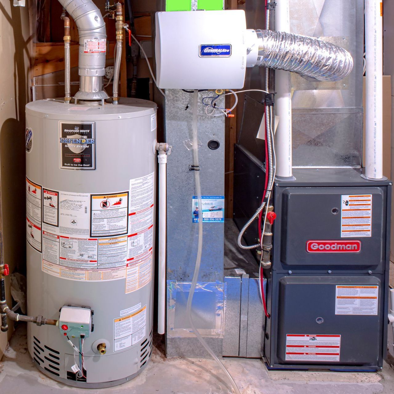 A furnace and water heater in a basement. The furnace is gray, and the water heater is silver, with connected ductwork.