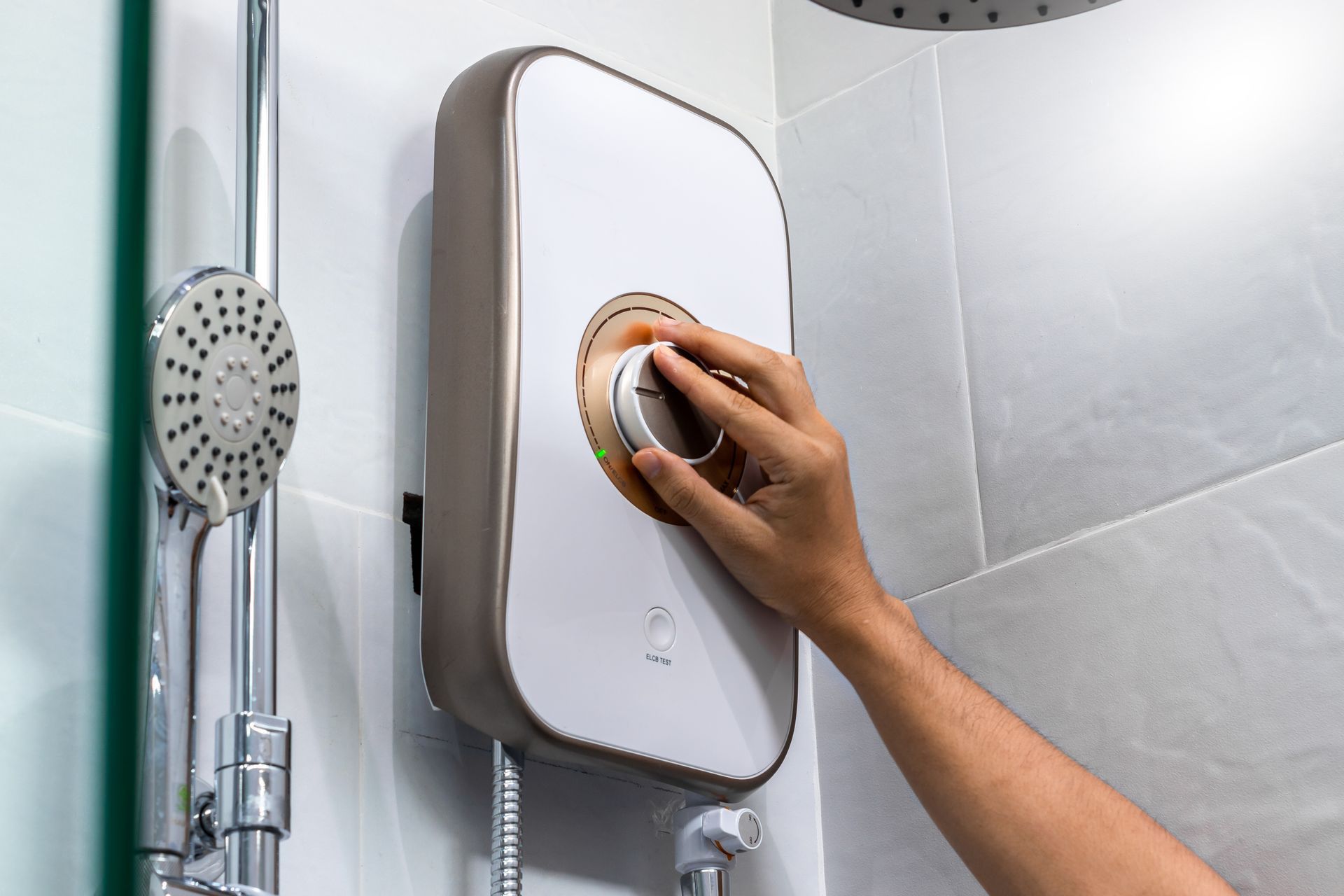 Person adjusting a shower water heater temperature dial in a tiled bathroom.