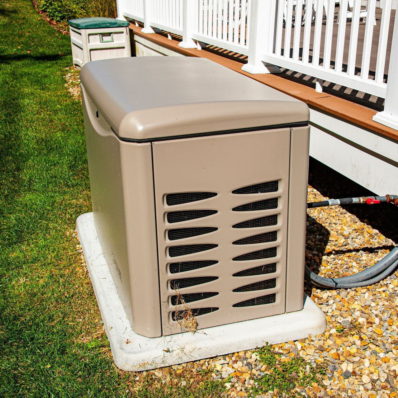 Tan generator unit on a concrete pad next to a house with a white porch.