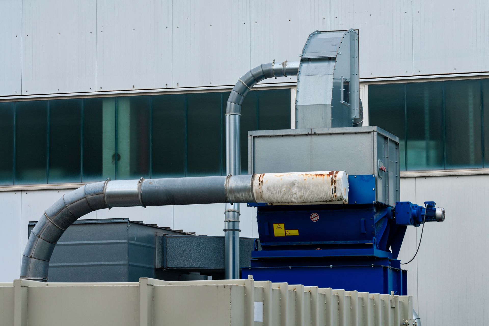 Industrial dust collection system on a building rooftop; metal ducts, blue machinery.