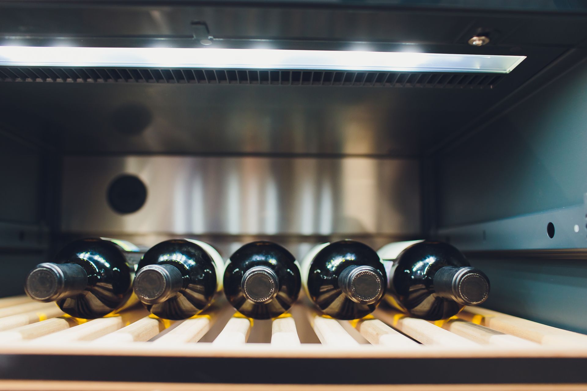 A row of wine bottles sitting on top of a wooden shelf in a wine cooler.