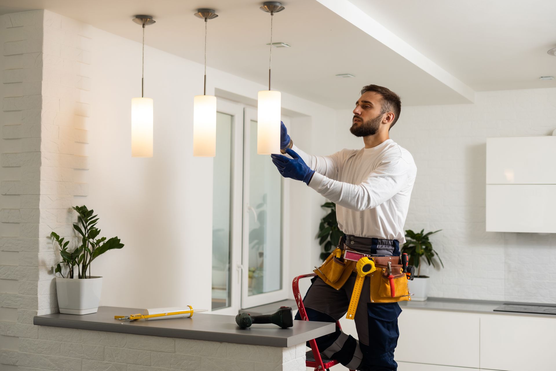 Un homme en tenue de travail installe un luminaire dans une cuisine moderne.