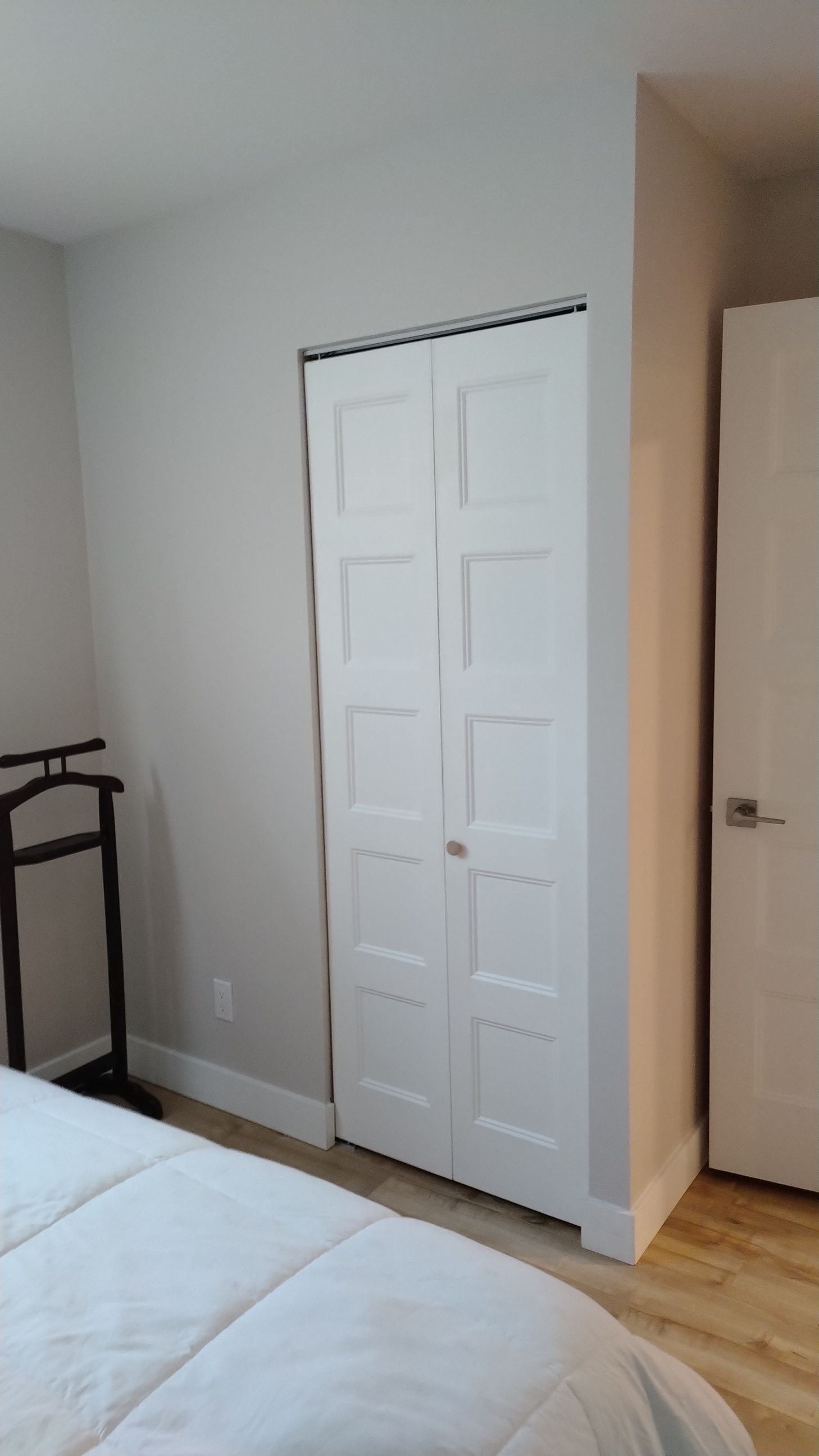 Portes de placard blanches pliantes dans une chambre avec un lit et un portant à vêtements sur pied.