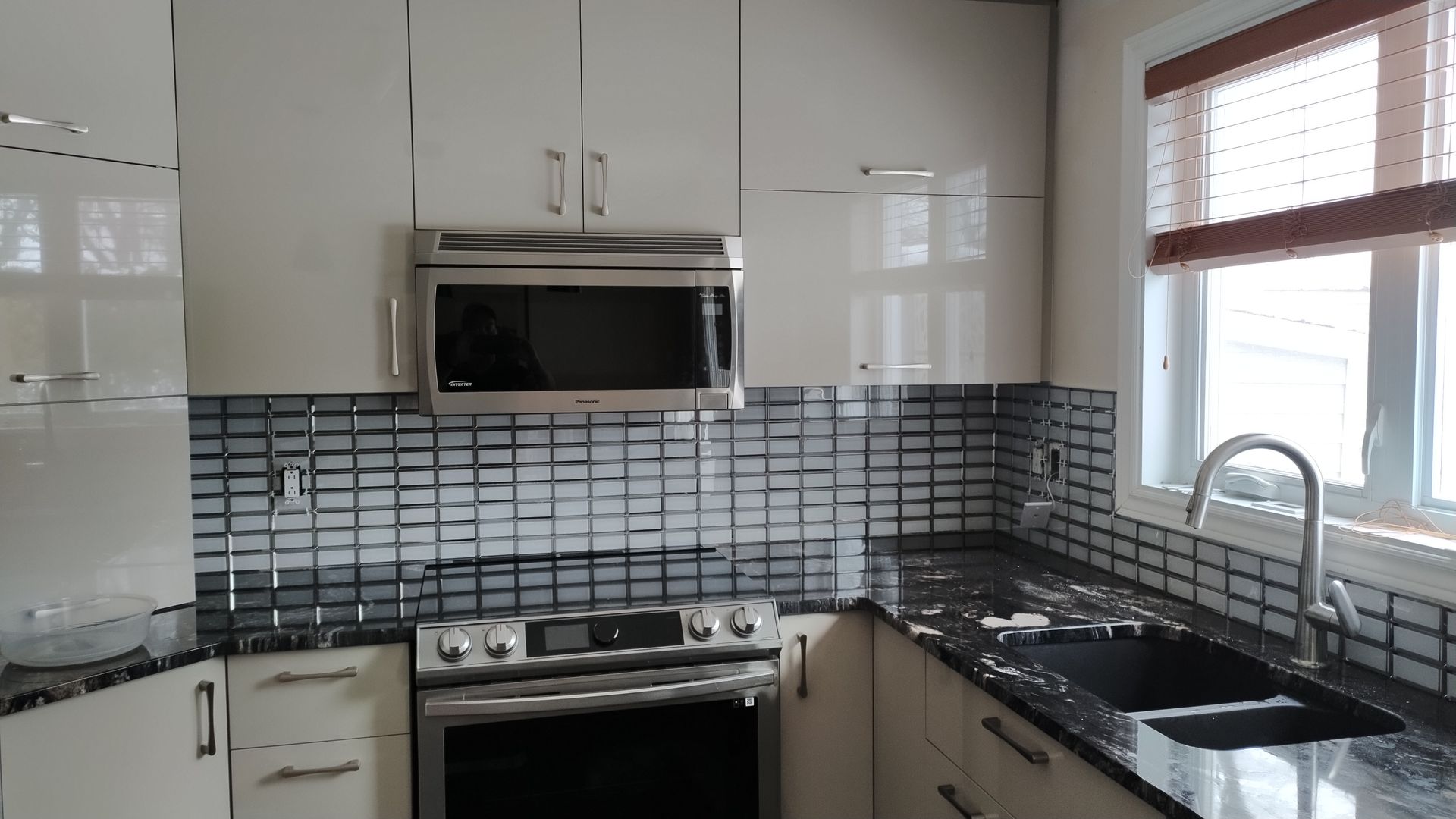 Cuisine moderne avec armoires blanches, comptoirs noirs et crédence en mosaïque. Électroménagers en acier inoxydable.