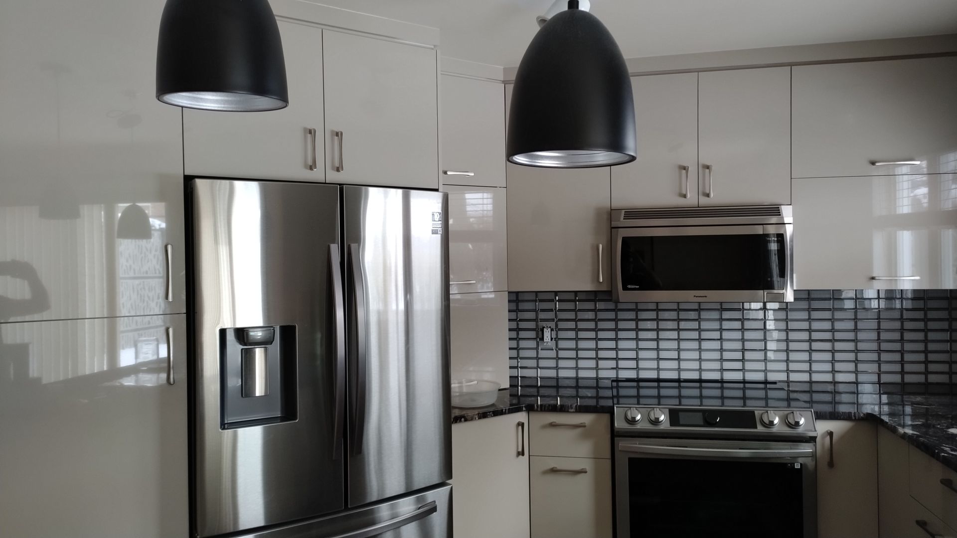 Cuisine moderne avec placards blancs, appareils électroménagers en acier inoxydable et suspensions lumineuses noires.