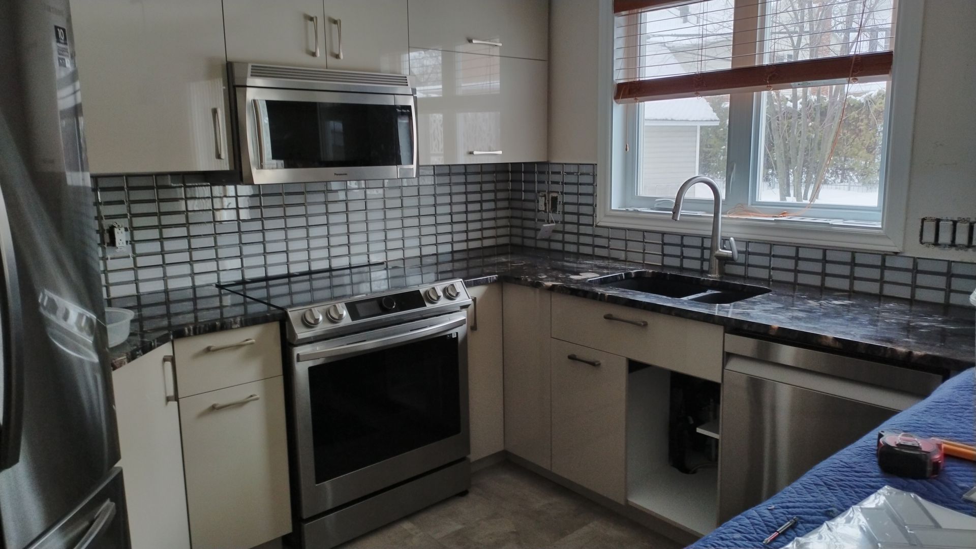 Cuisine moderne avec appareils électroménagers en acier inoxydable, comptoir foncé et crédence carrelée.