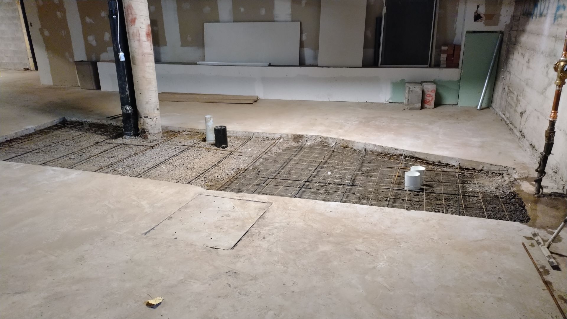 Sous-sol en construction ; armatures et plomberie apparentes, béton coulé par sections.