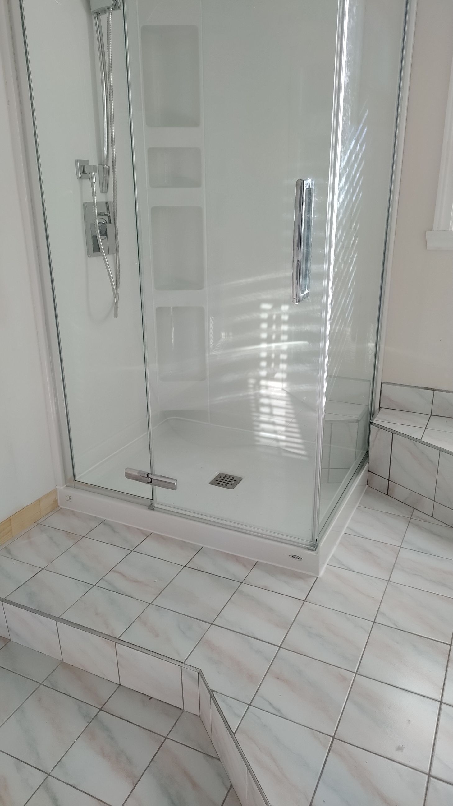 Cabine de douche en verre dans une salle de bains avec sol en carrelage de marbre blanc et une marche.