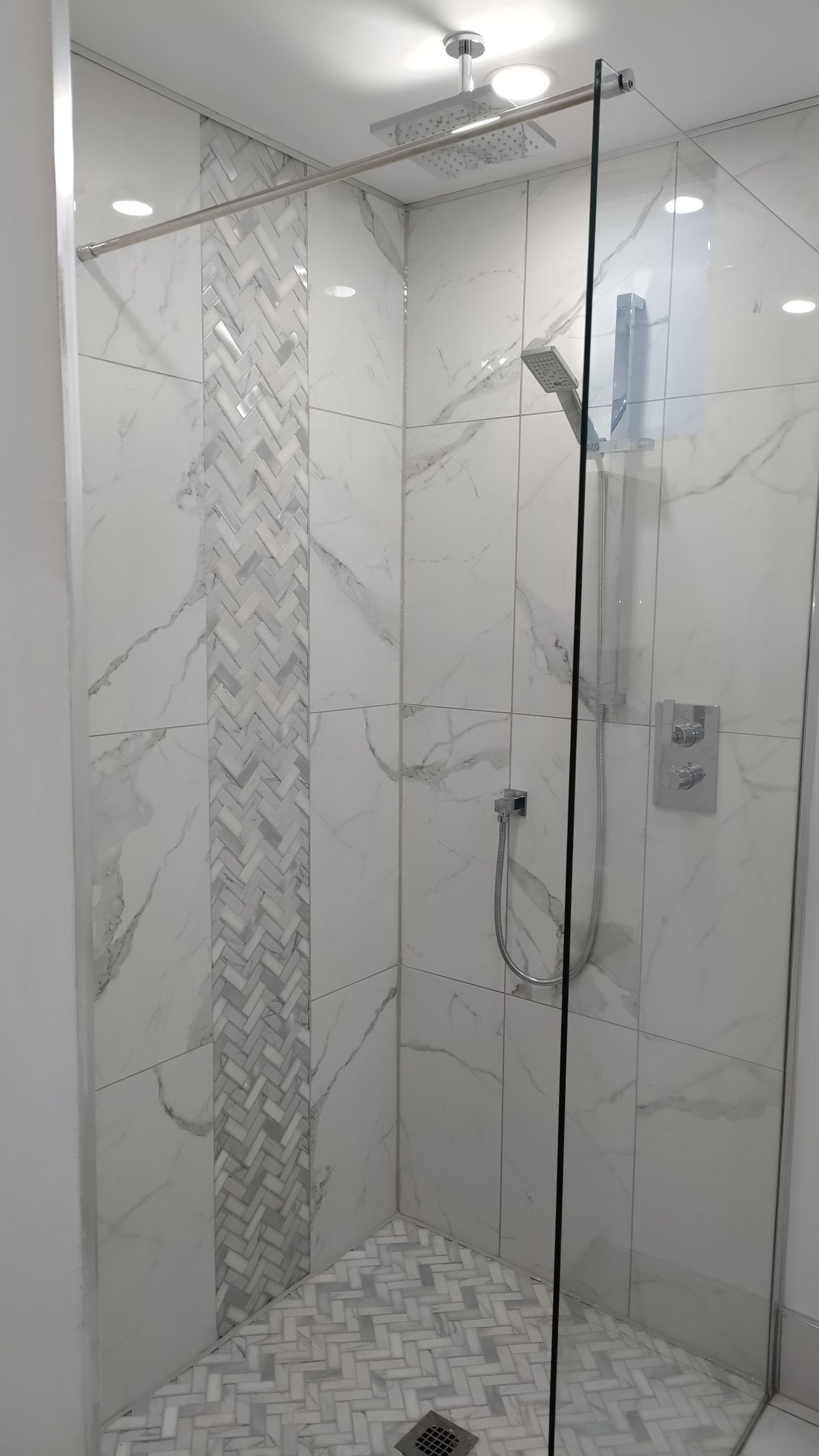 Douche avec carrelage en marbre blanc et porte en verre. Décorée d'un carrelage à chevrons.