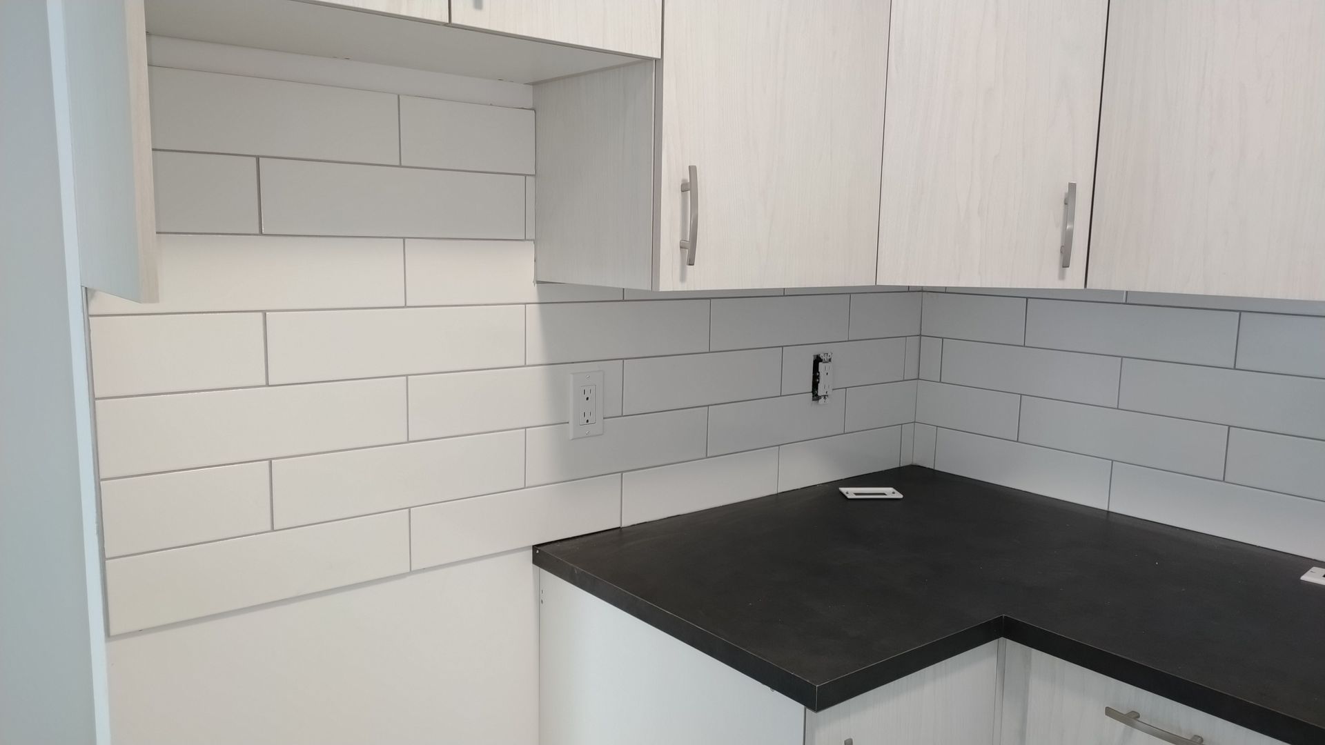 Cuisine blanche avec crédence en carrelage métro, plan de travail foncé et placards blancs.