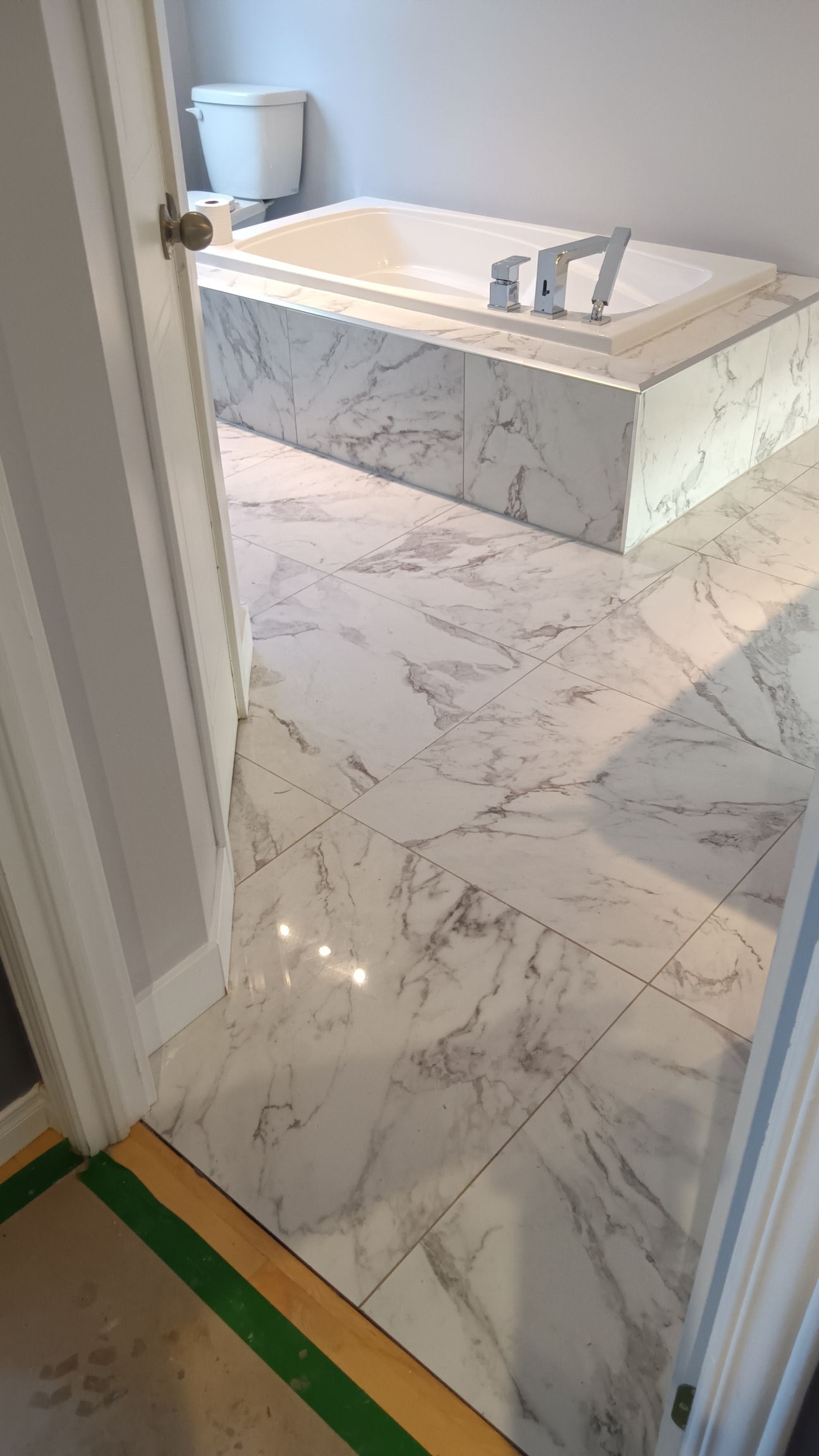 Salle de bains avec sol et baignoire en marbre blanc, vue depuis la porte.