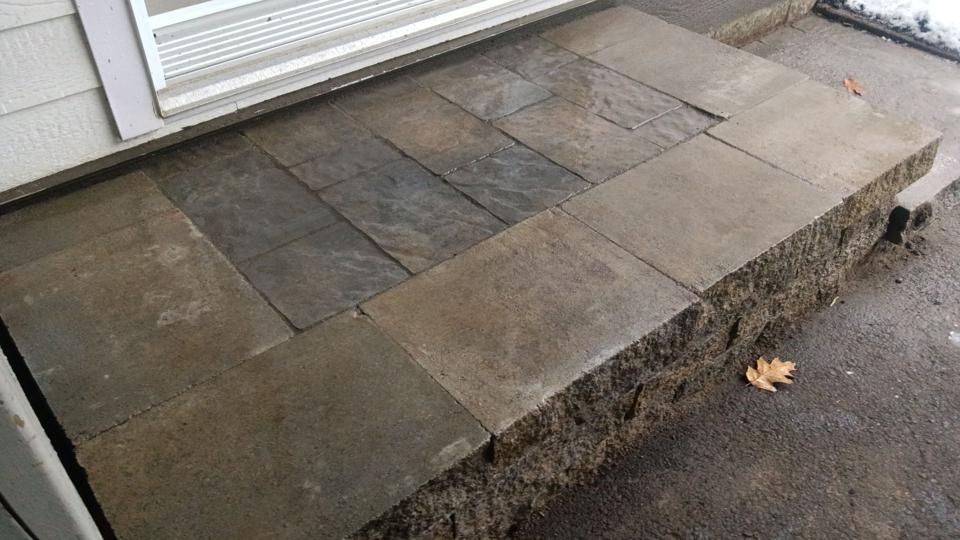 Marche en pierre avec pavés gris foncé, menant à une porte au bardage clair.