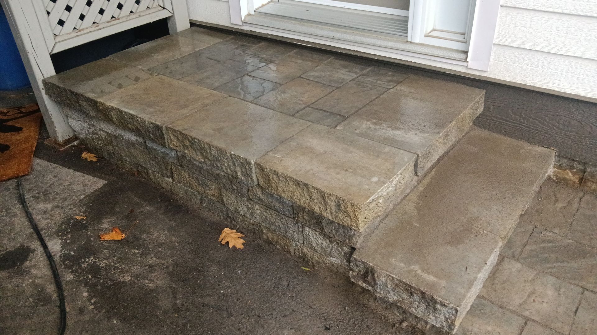 Marches en pierre menant à une porte, surface humide, tons gris clair et bruns.