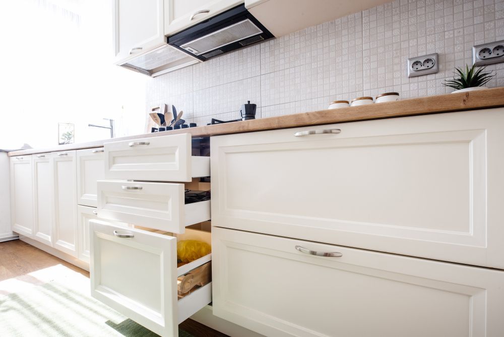Modern white kitchen with open drawers, wooden countertop, built-in stovetop, and tile backsplash.