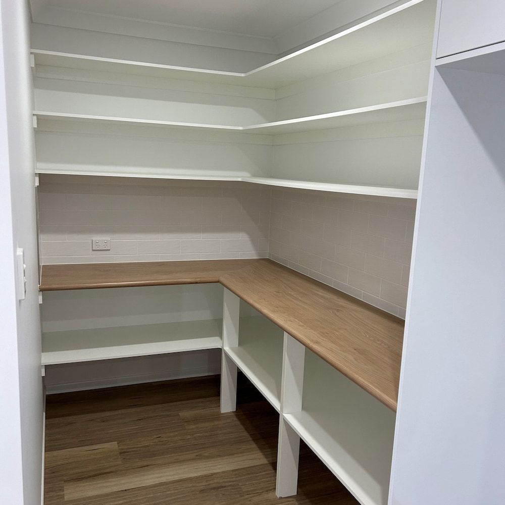A Walk In Pantry With White Shelves And A Wooden Table — Pioneer Cabinets in Moranbah, QLD