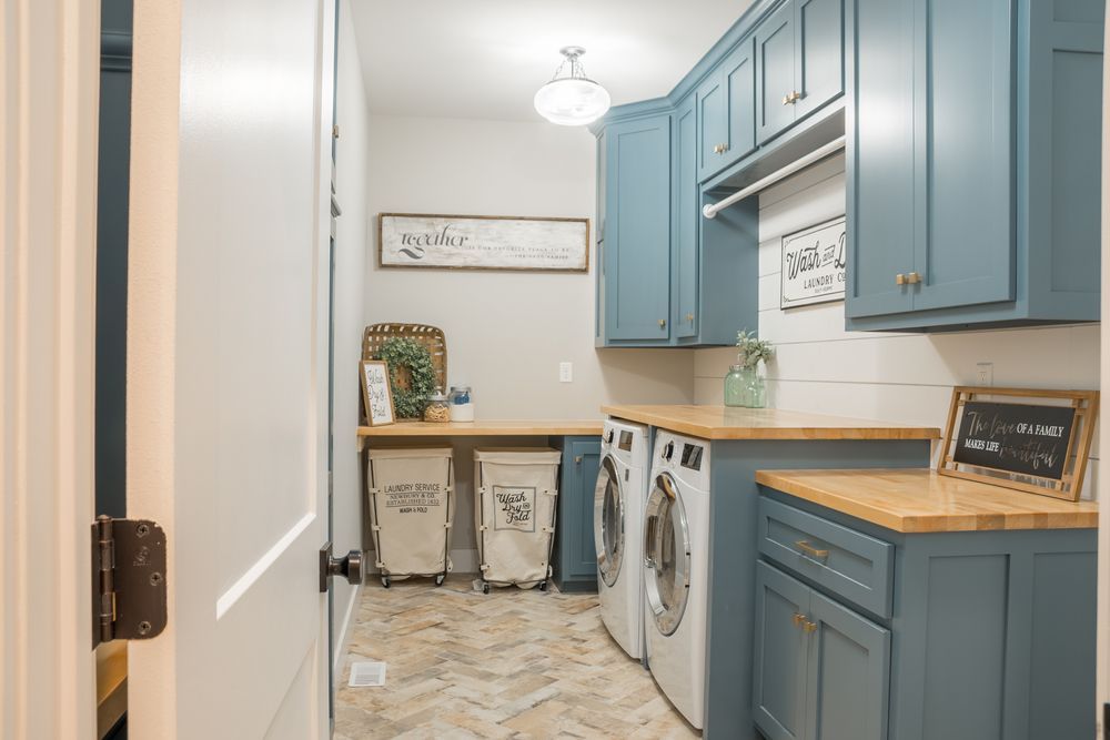Modern laundry room with blue cabinets, butcher block countertops, front-load washer and dryer.