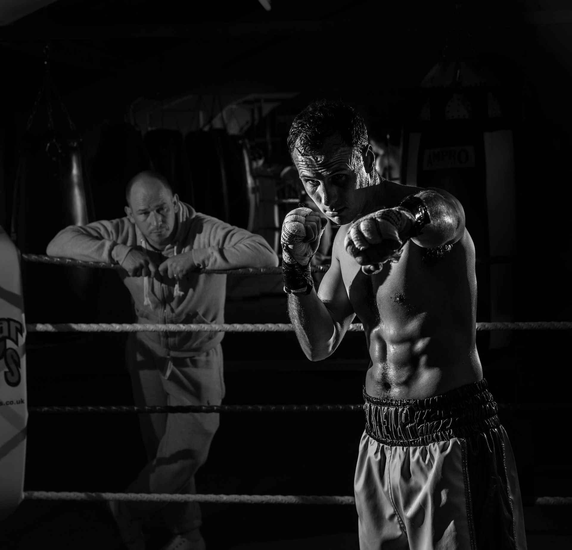 A man is standing in a boxing ring while another man watches
