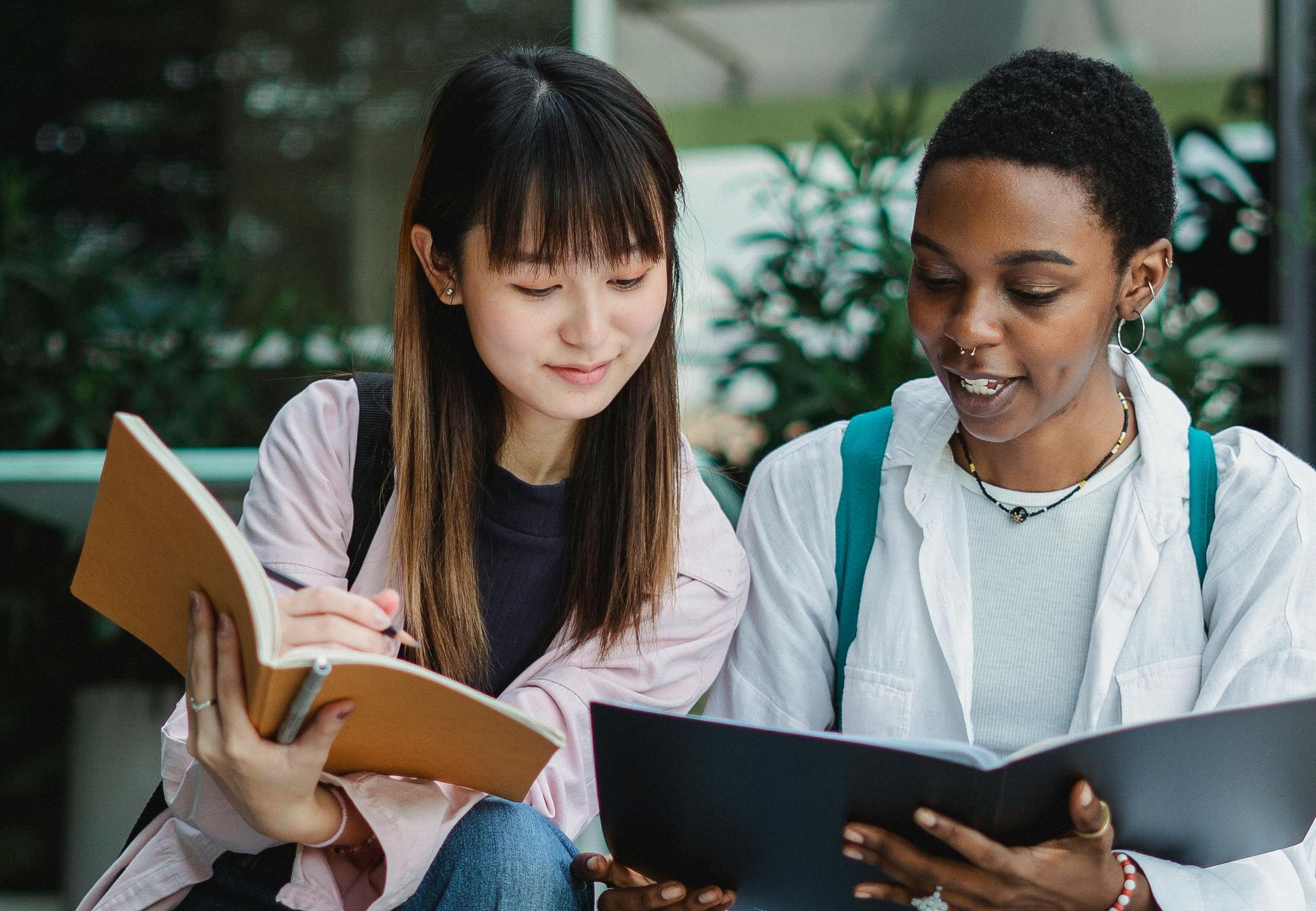 two woman are sitting next to each other reading books.