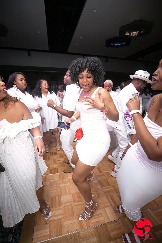 A group of people in white dresses are dancing on a wooden floor.