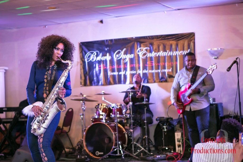 A woman is playing a saxophone and a man is playing a guitar on stage.