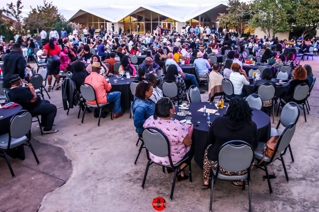 A large group of people are sitting at tables outside of a building.