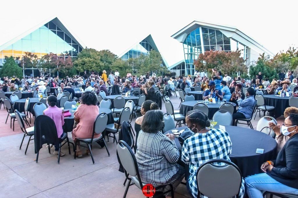 A group of people are sitting at tables in front of a large crowd.